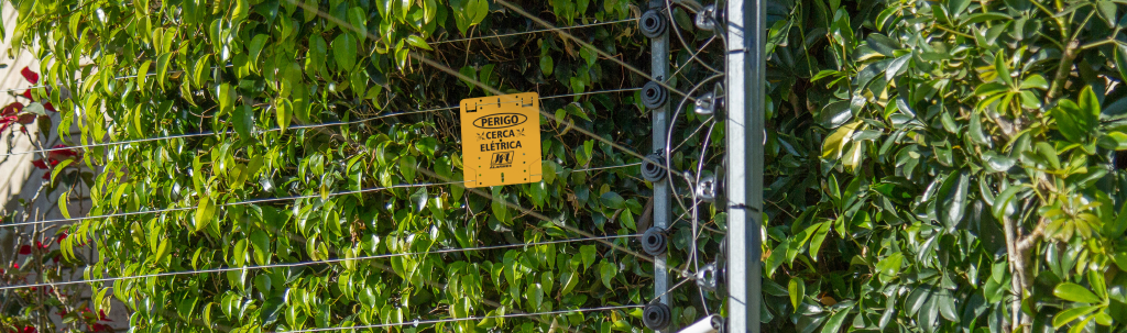 Cerca elétrica instalada, com hastes metálicas, isoladores e placa de advertência